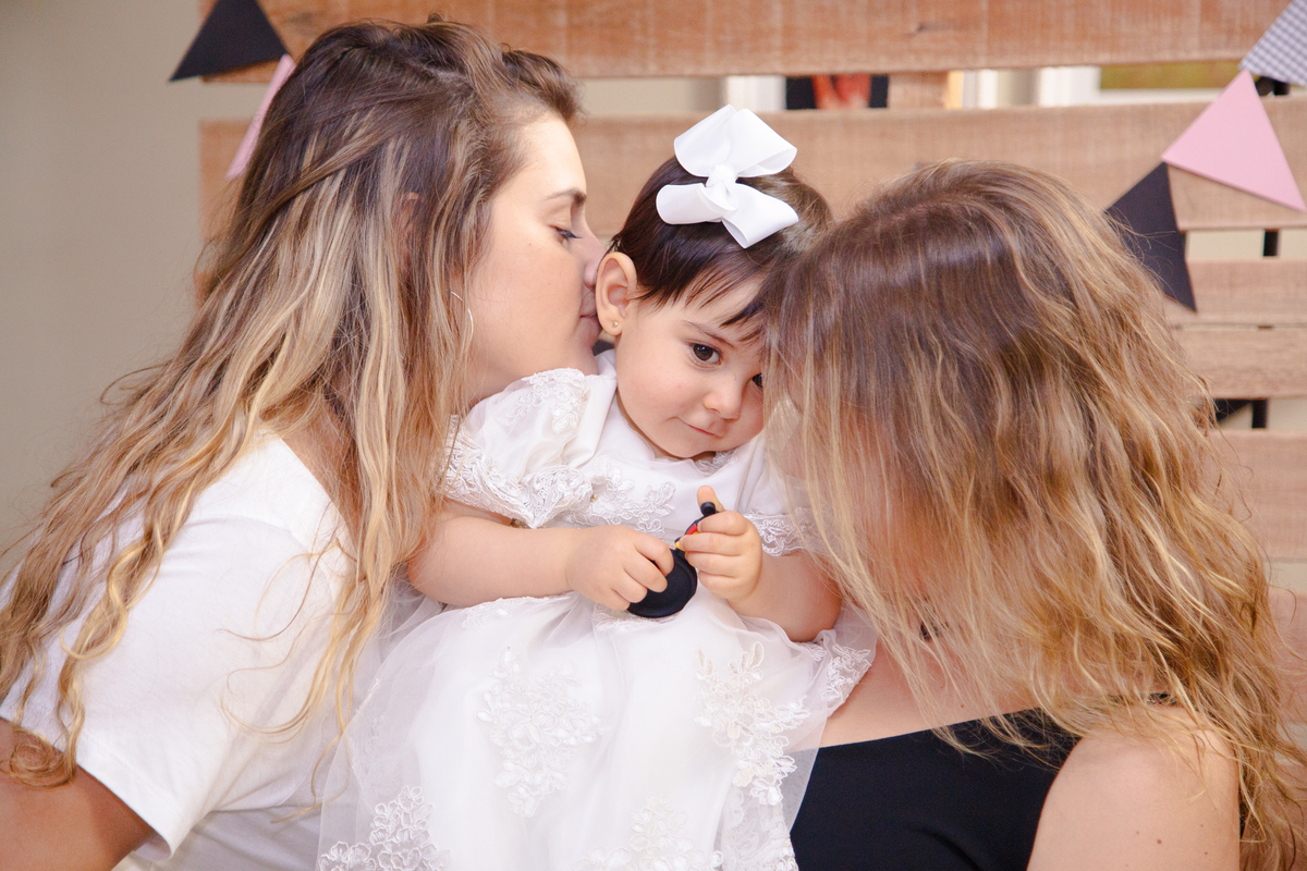 Bebê no colo de duas primas e ganhando um cheiro no pescoço de uma delas.