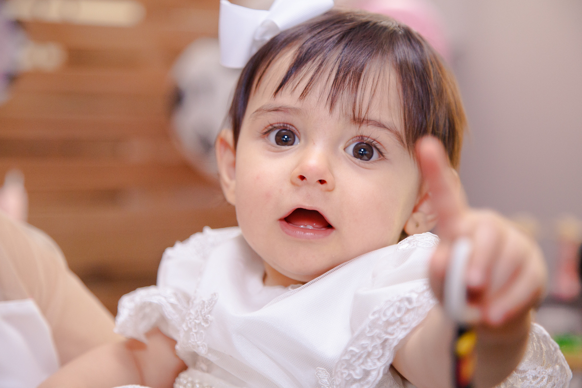 Close no rosto da bebê, que está completando um ano, ela sorri e aponta para a câmera.