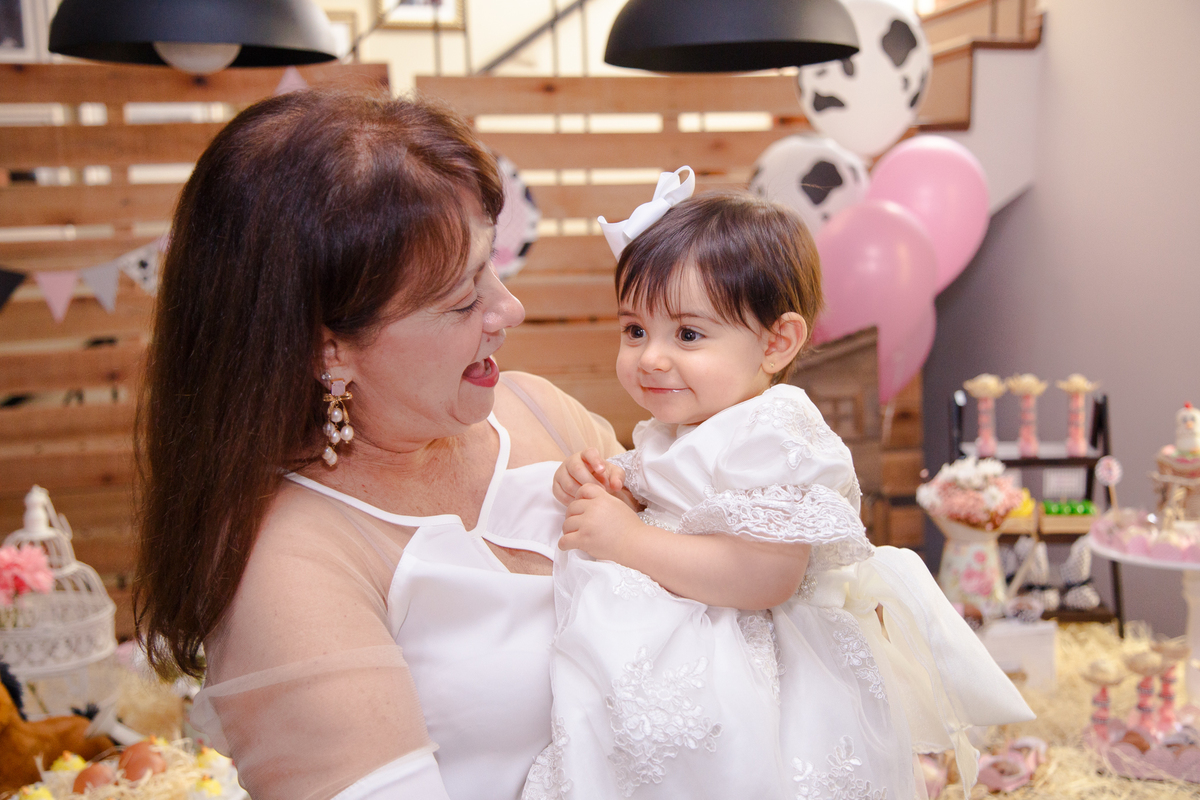 Bebê no colo de sua avó brincando em seu aniversário de 1 ano. Ambas sorriem.