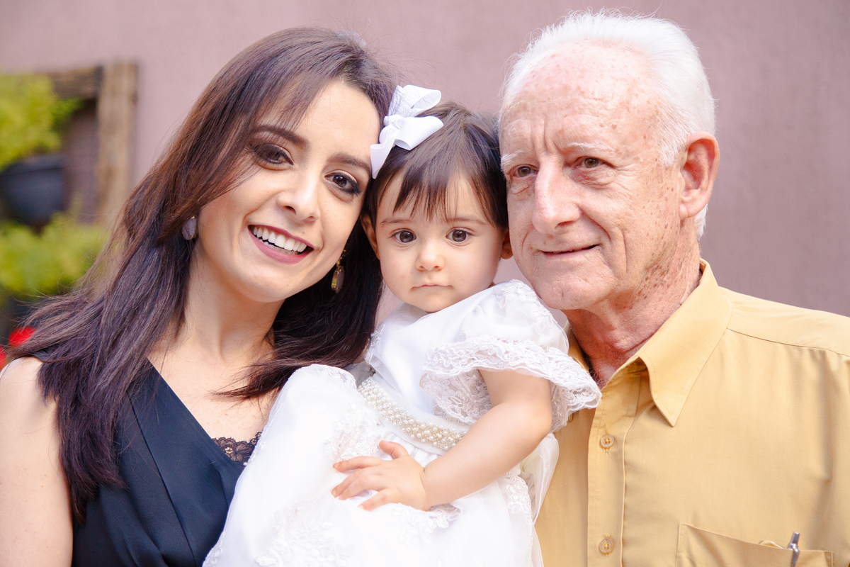 Três gerações, bebê com sua mãe e seu avô materno posando para uma foto no aniversário de um ano da bebê.