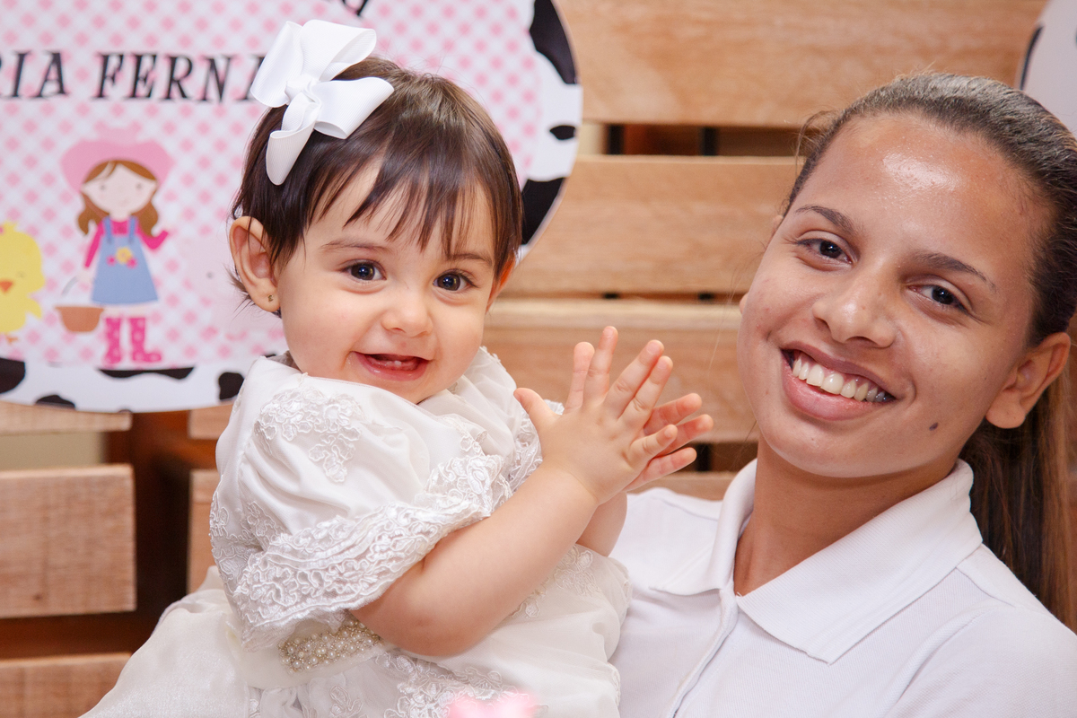 Bebê no colo de sua babá sorrindo para a câmera e batendo palminhas.