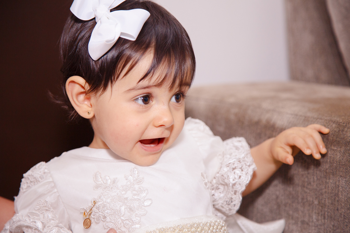 Close de uma bebê apoiada no sofá interagindo com alguém que não aparece na foto, com uma expressão como se estivesse conversando.