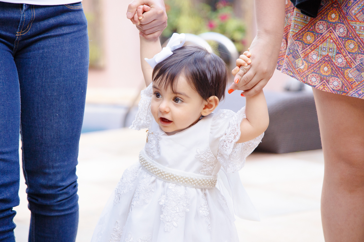 Bebê de mão dada com duas pessoas, andando em sua festa de aniversário de 1 ano.