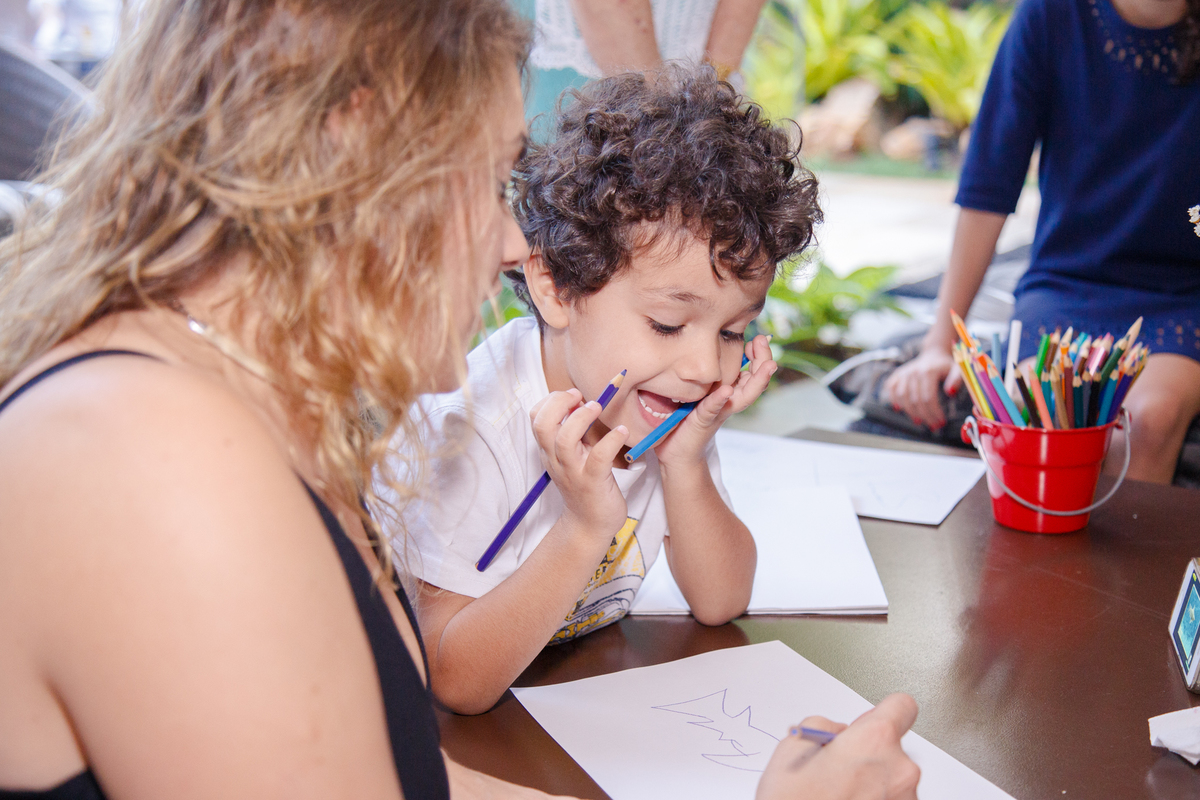 Criança brincando de desenhar com sua prima, com lápis de cor na mão e uma expressão alegre.