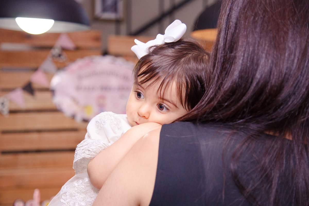 Bebê deitada no ombro de sua mãe já cansada após sua festa de aniversário de 1 ano.