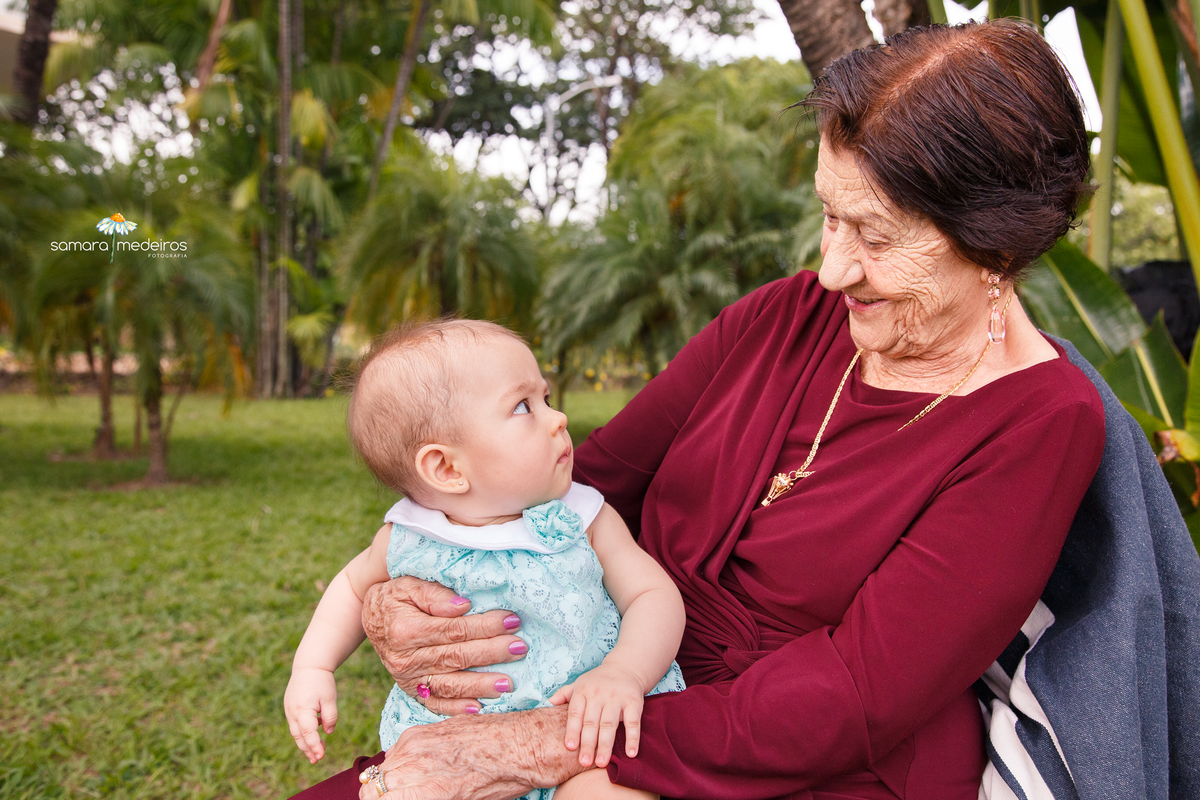 Senhora sentada em uma cadeira com a bisneta sentada em seu colo e ambas se observando.
