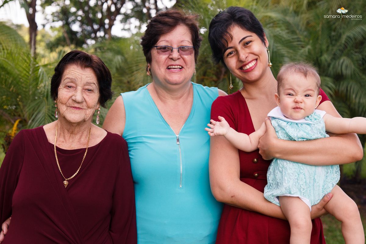 Quatro gerações, mãe, filha, neta e bisneta, todas olhando para a câmera sorrindo, e a bebê fazendo uma careta engraçadinha.
