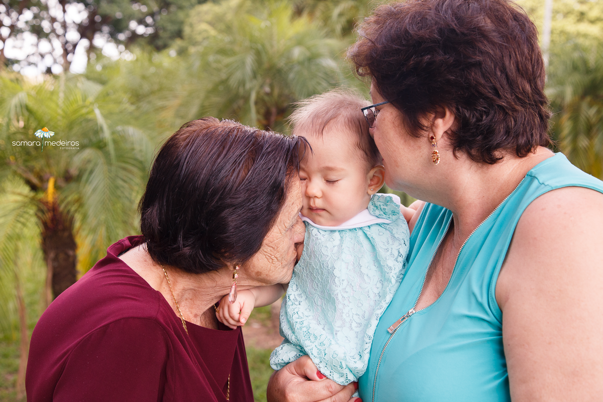 Bebê no colo da avô, com os olhinhos fechados,  e ganhando um cheiro da avô e da bisavó.