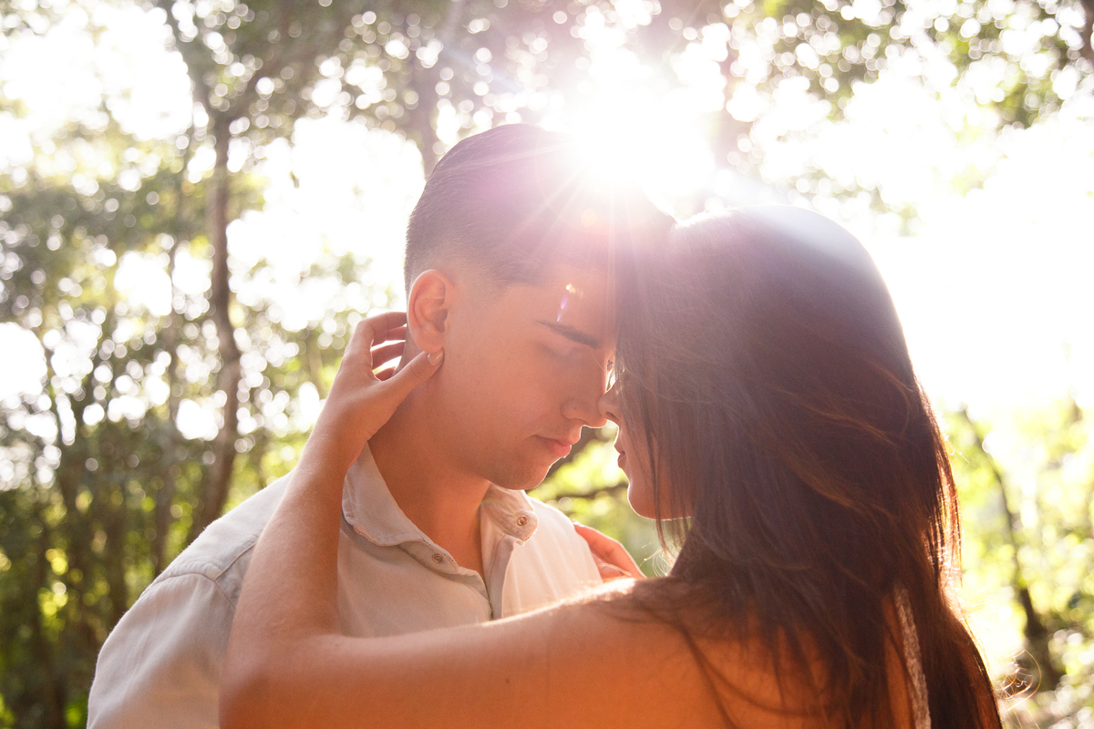 Foto de um casal com as testas se encontrando e o sol ao fundo dando um reflexo atrás da cabeça deles.