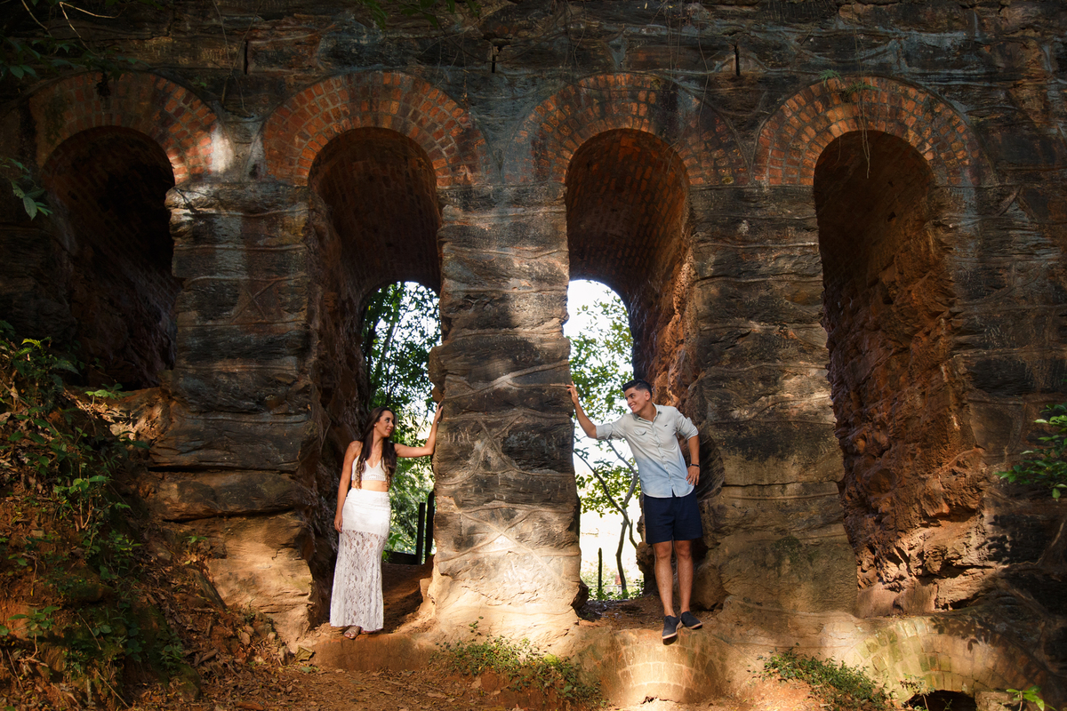 Foto de um casal em uma ruína de trilhos de trem se olhando, cada um dos dois em um vão da ruína.
