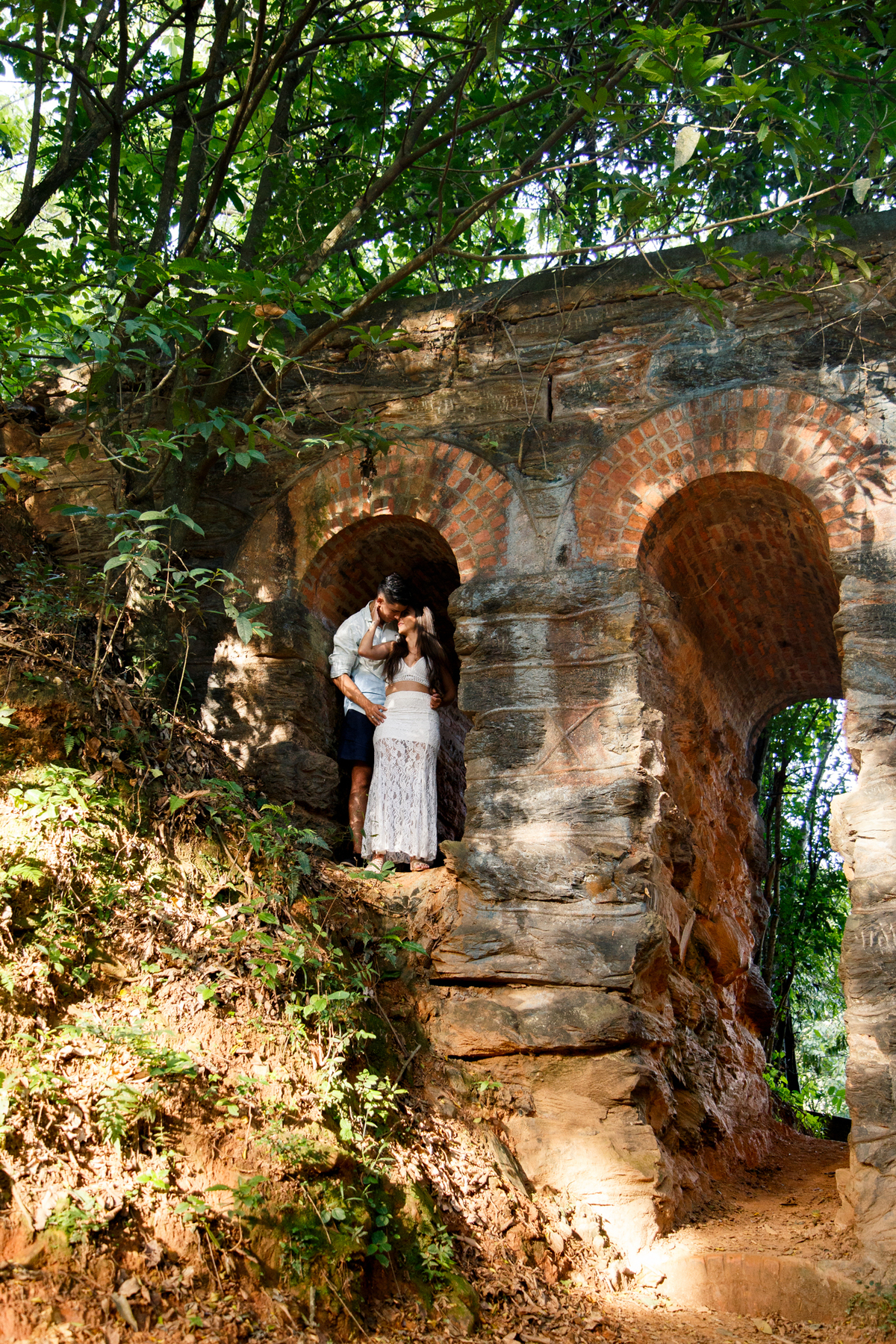 Casal abraçado e se olhando em um vão abaixo dos trilhos de trem em ruína em uma cidade próxima a Belo Horizonte.