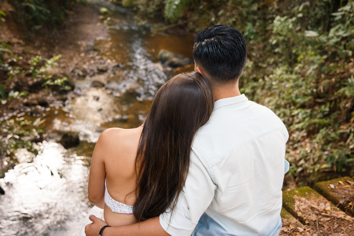 Casal sentado, lado a lado, se abraçando e observando a paisagem enquanto posam para uma sessão de fotos de casal.
