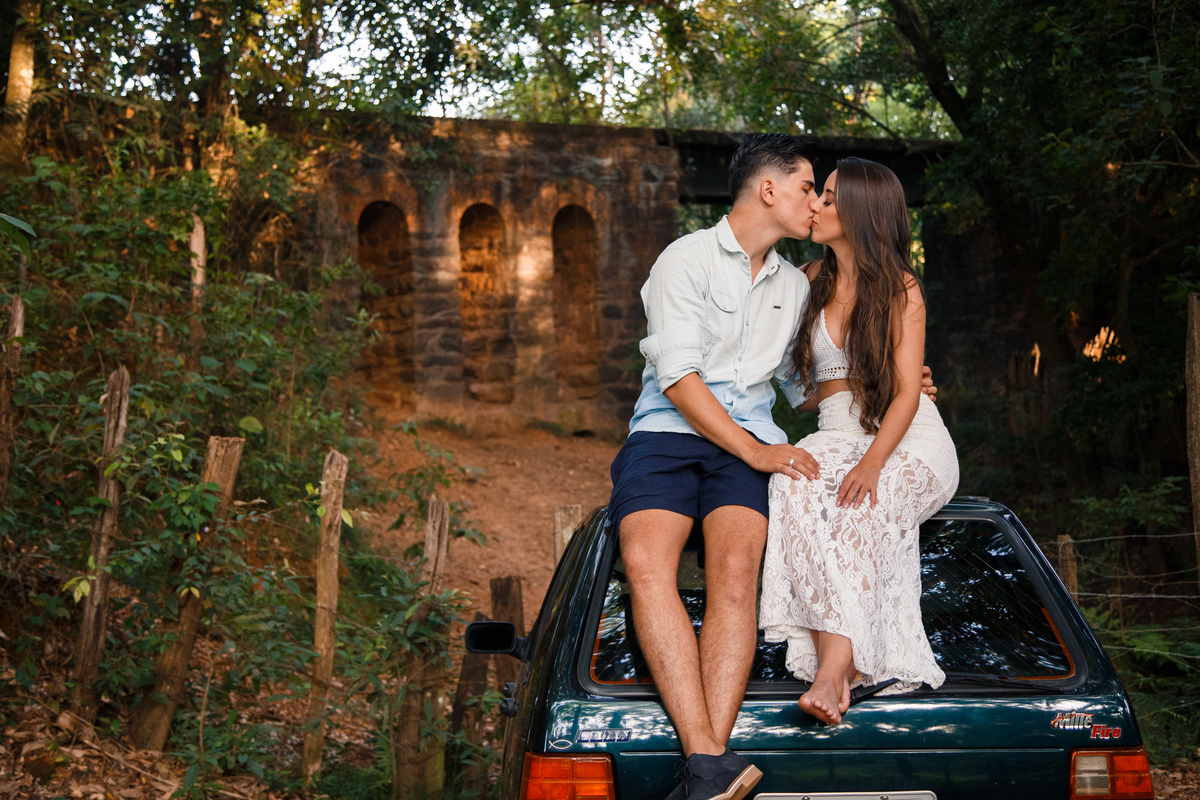 Casal se beijando sentados no teto do carro deles, que consideram especial, com as ruínas de um trilho de trem abandonado ao fundo.
