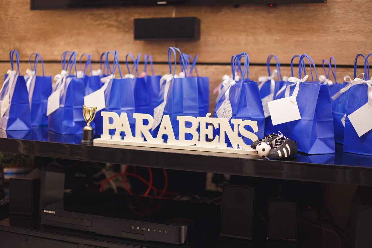 Detalhe das lembrancinhas para os convidados com uma placa de parabéns em frente às sacolas de papel azul com os doces.