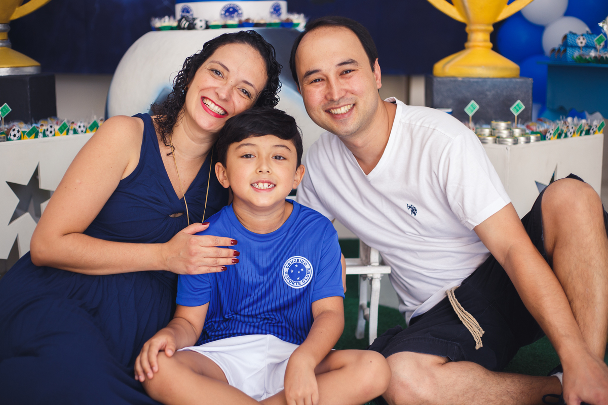 Mãe e pai com o filho aniversariante, sentados no chão na frente da mesa do bolo.