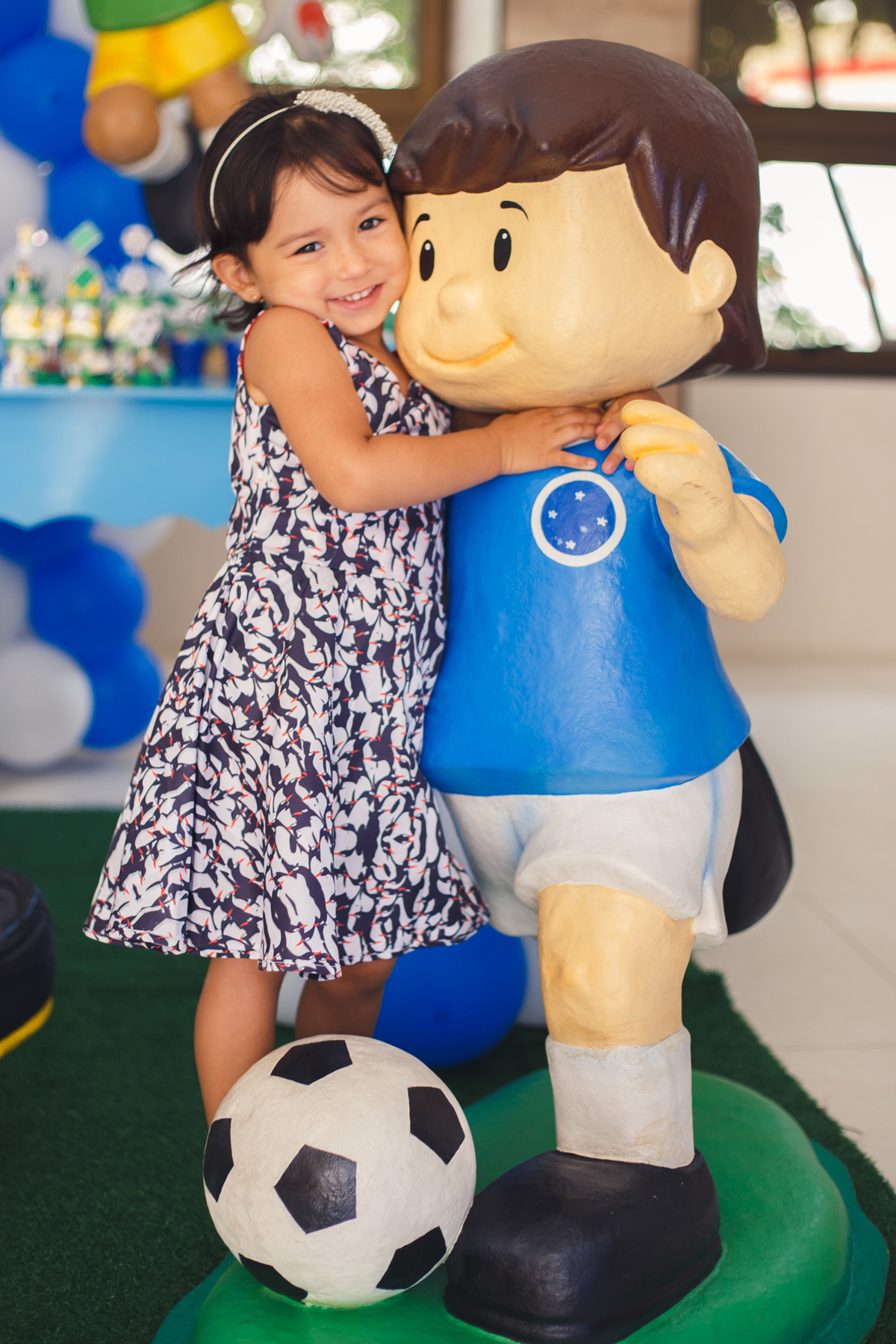 Irmã mais nova do aniversariante abraçando o boneco com camisa do cruzeiro que decora a festa.