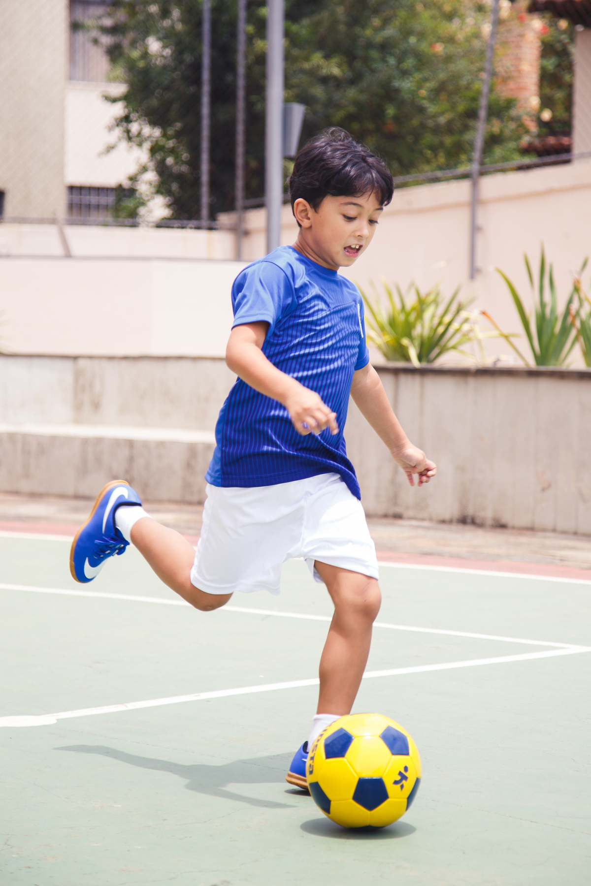 Criança que está fazendo aniversário brincando durante a festa, jogando futebol, correndo e preparando um chute.