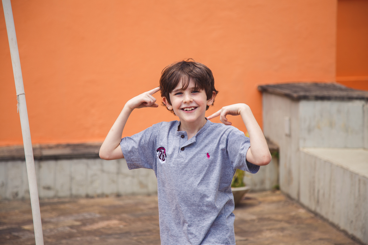 Criança comemorando um gol fazendo movimentos circulares com os dedos indicadores ao redor da orelha e sorrindo para a foto.