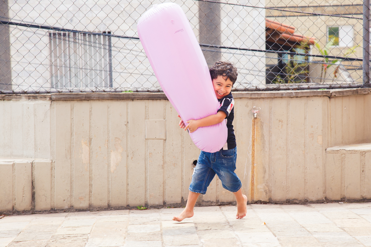 Criança correndo abraçada a um joão bobo e dando uma gargalhada.
