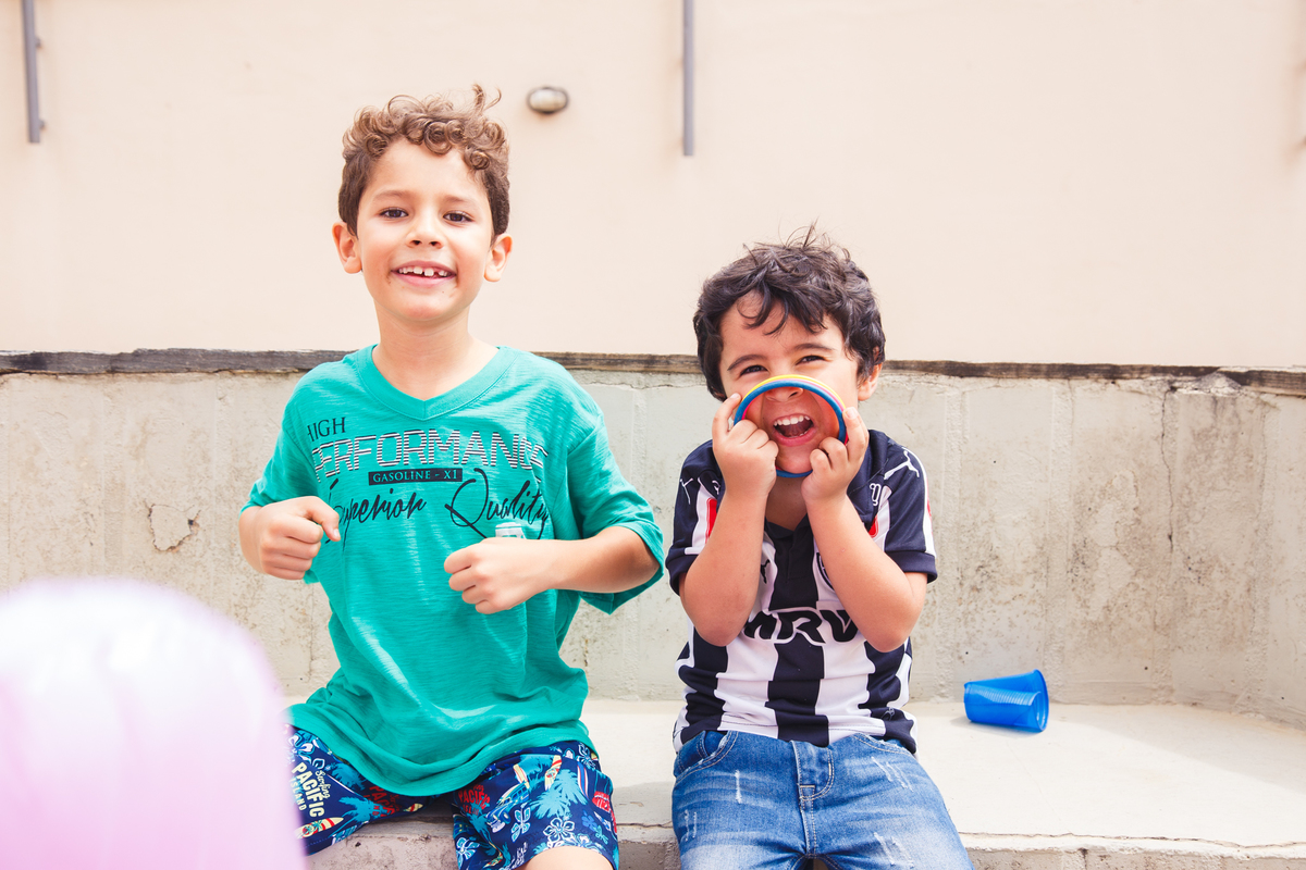 Duas crianças sentadas em um banco de cimento, fazendo careta para a foto, durante aniversário infantil, em Belo Horizonte.