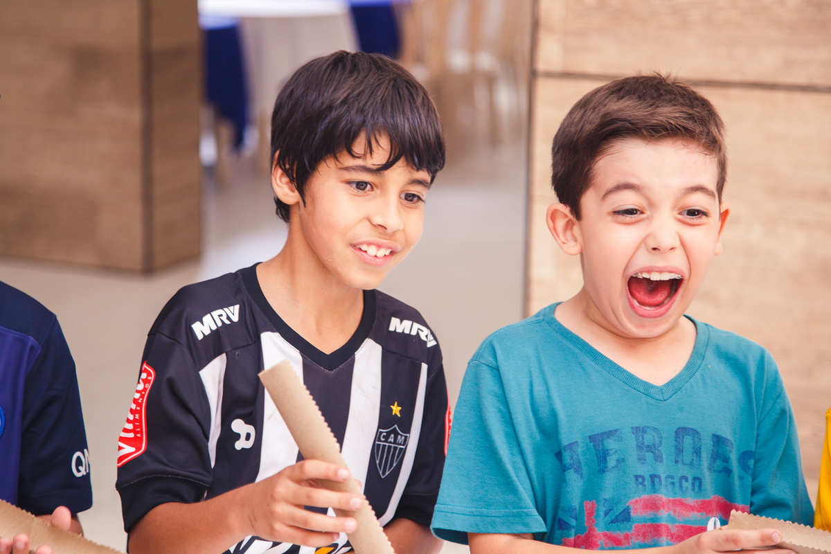 Duas crianças durante uma brincadeira em uma festa de aniversário, um com um leve sorriso e outro com uma enorme gargalhada.