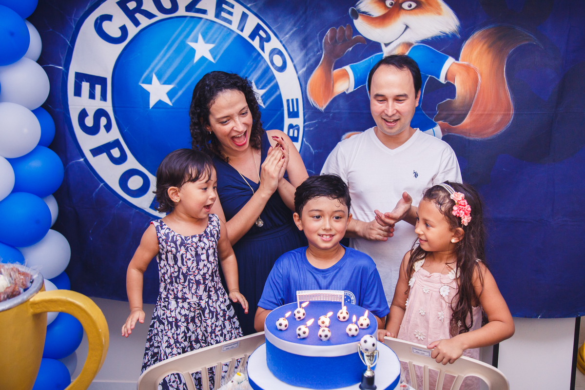 Família, mãe, pai e três irmãos, reunida atrás da mesa do bolo durante o parabéns.