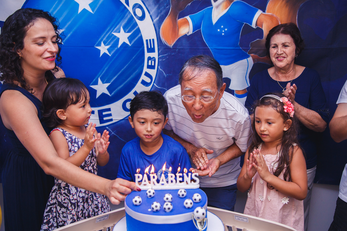 Avô da criança aniversariante soprando as velas após parabéns para ele.
