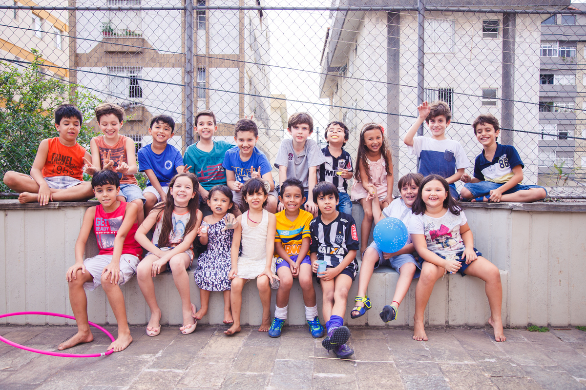 Todas as crianças da festa de aniversário reunidas, sentadas em um banco de cimento posando para uma foto no fim da festa.