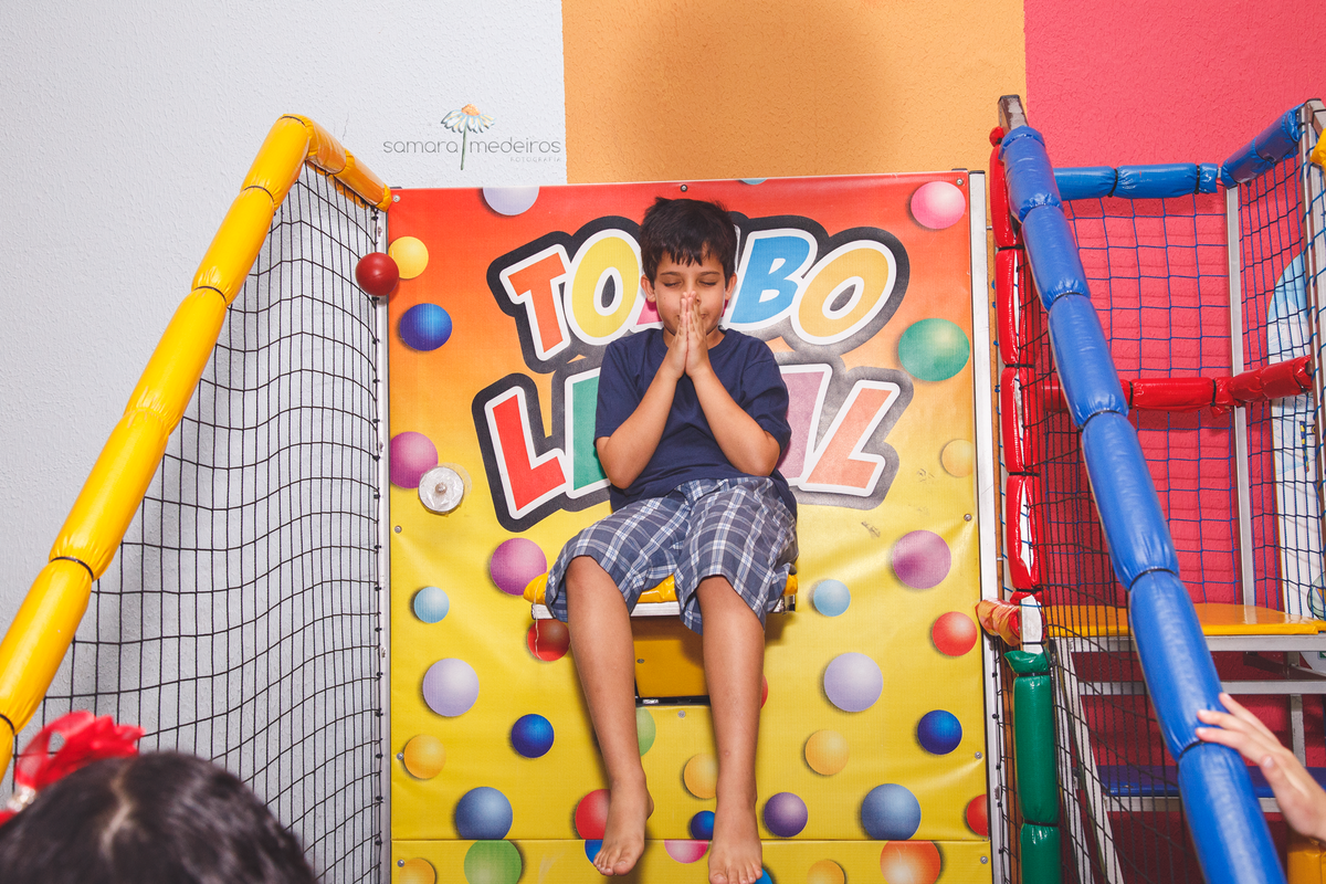 Criança sentada no brinquedo tombo legal, brincando com as mãos em posição de oração.