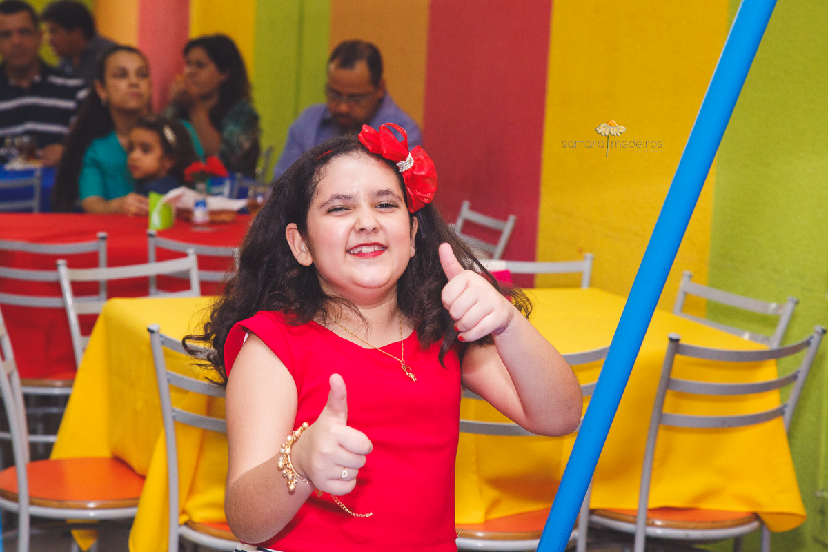 Criança aniversariante brincando e fazendo gracinha para a foto, dançando e erguendo o polegar.