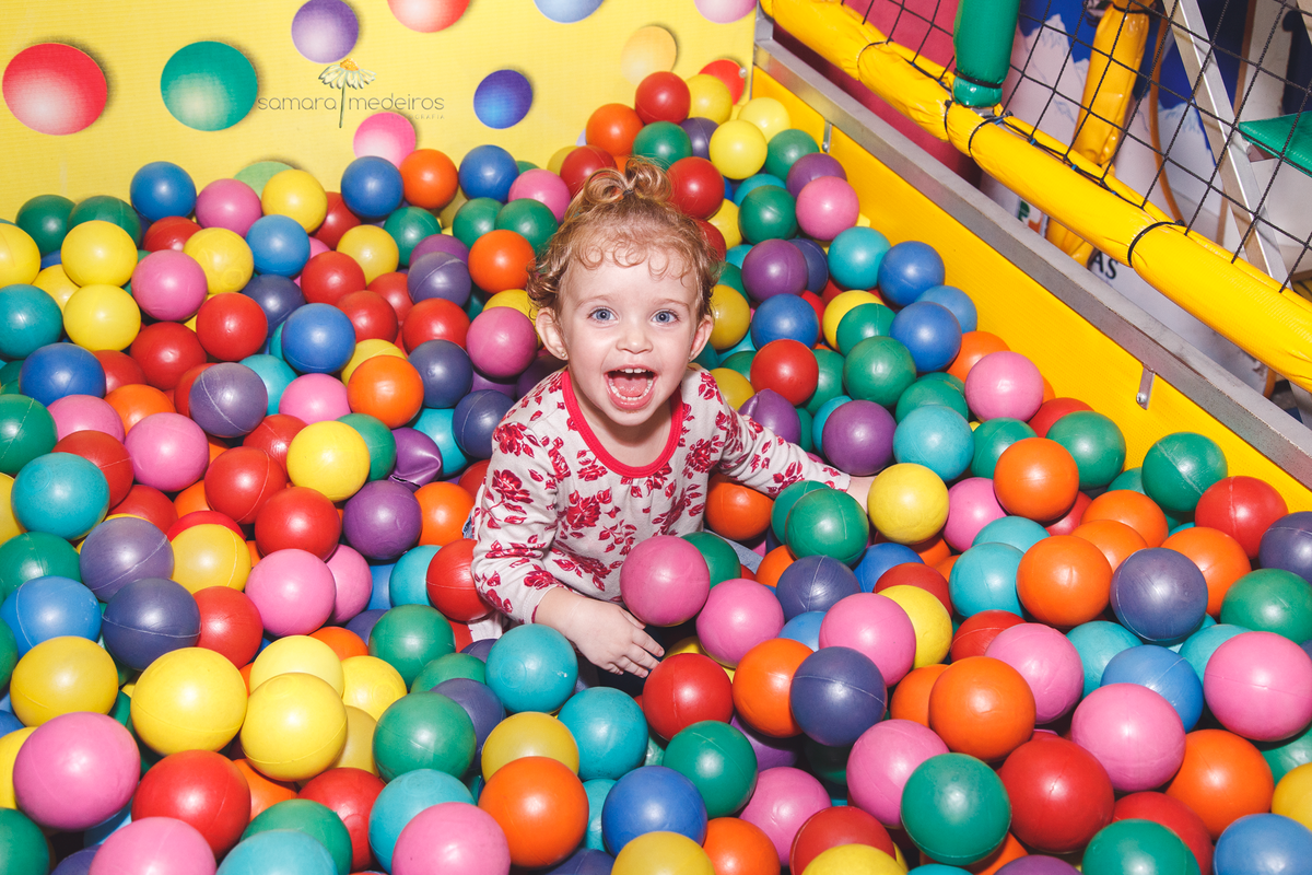 Criança dentro da piscina de bolinha, com um sorriso enorme, em uma festa de aniversário infantil.