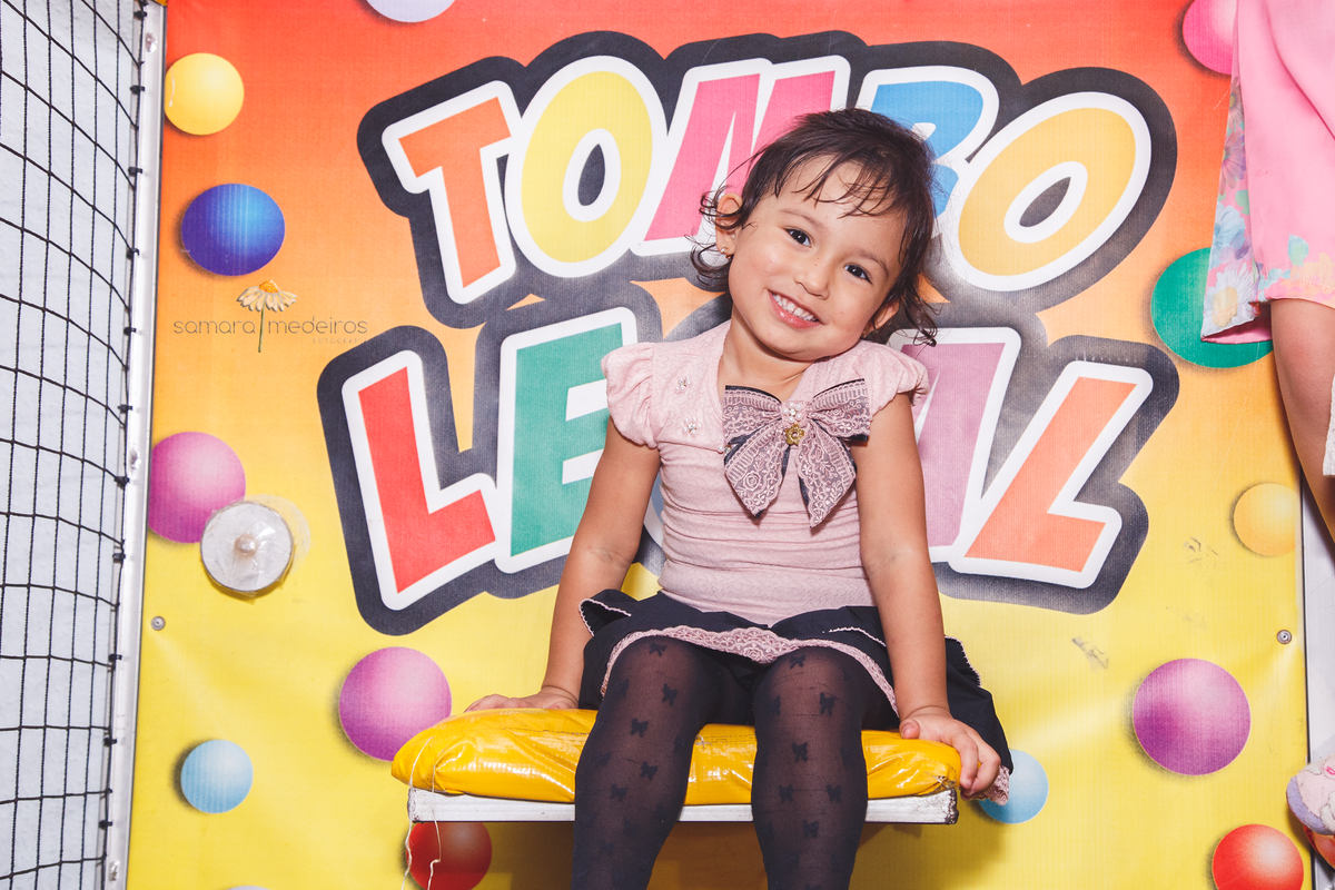 Criança sentada com uma pose meiga, na plataforma do brinquedo tombo legal.