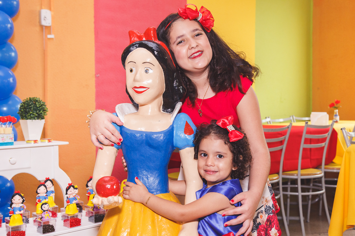 Duas irmãs aniversariantes abraçadas e abraçando a Branca de Neve que decora sua festa de aniversário.