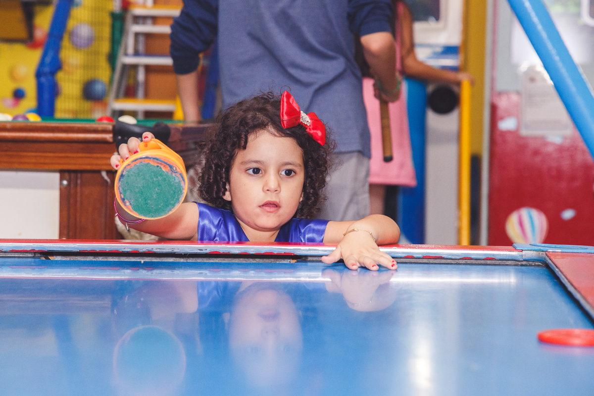 Criança brincando com um brinquedo de jogar um disco sobre uma mesa e tentar fazer gol do outro lado.