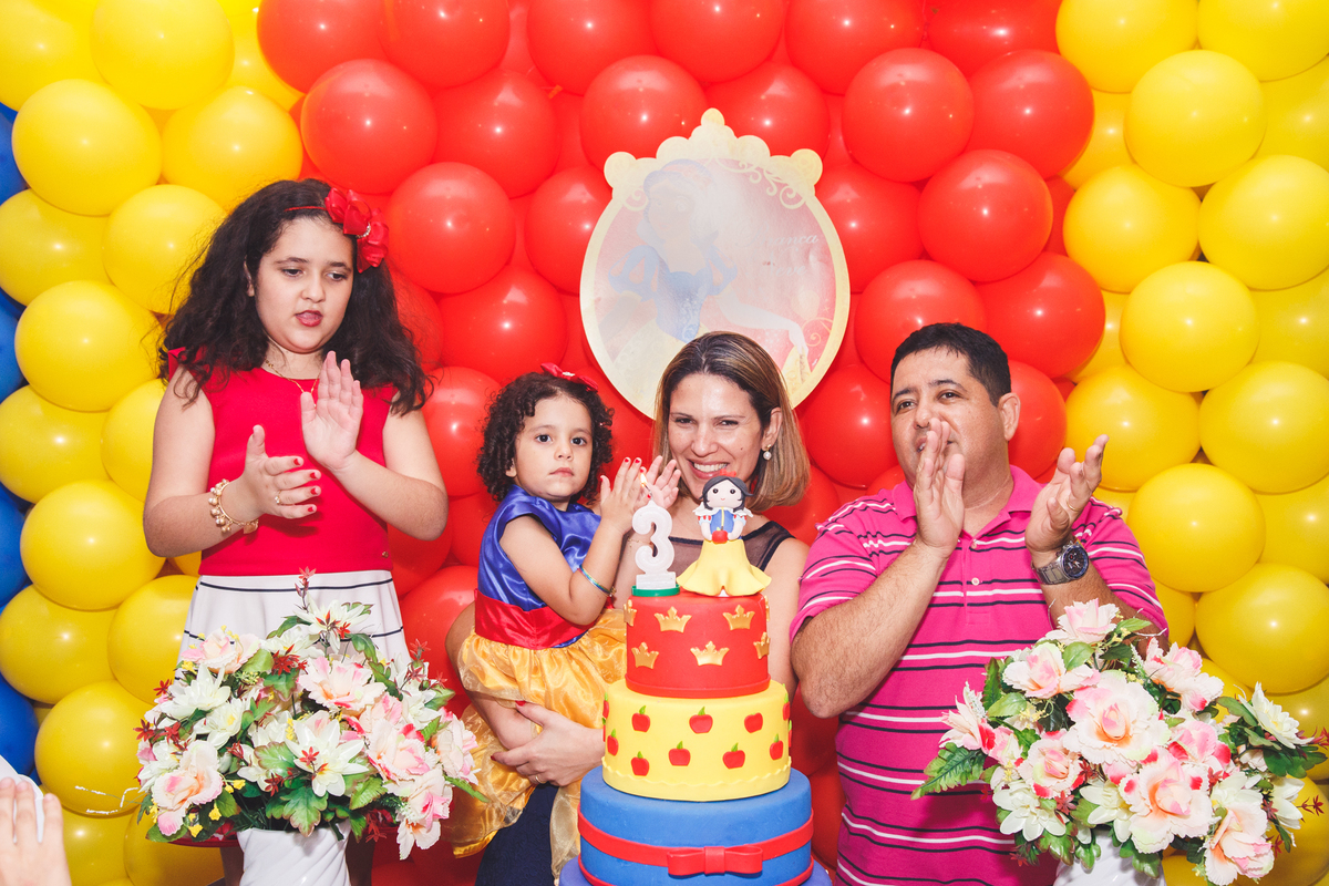 Mãe, pai e as duas filhas atrás da mesa do bolo cantando parabéns no aniversário das meninas.