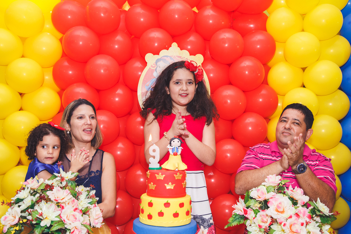 Mãe, pai e duas crianças cantando parabéns atrás da mesa do bolo.