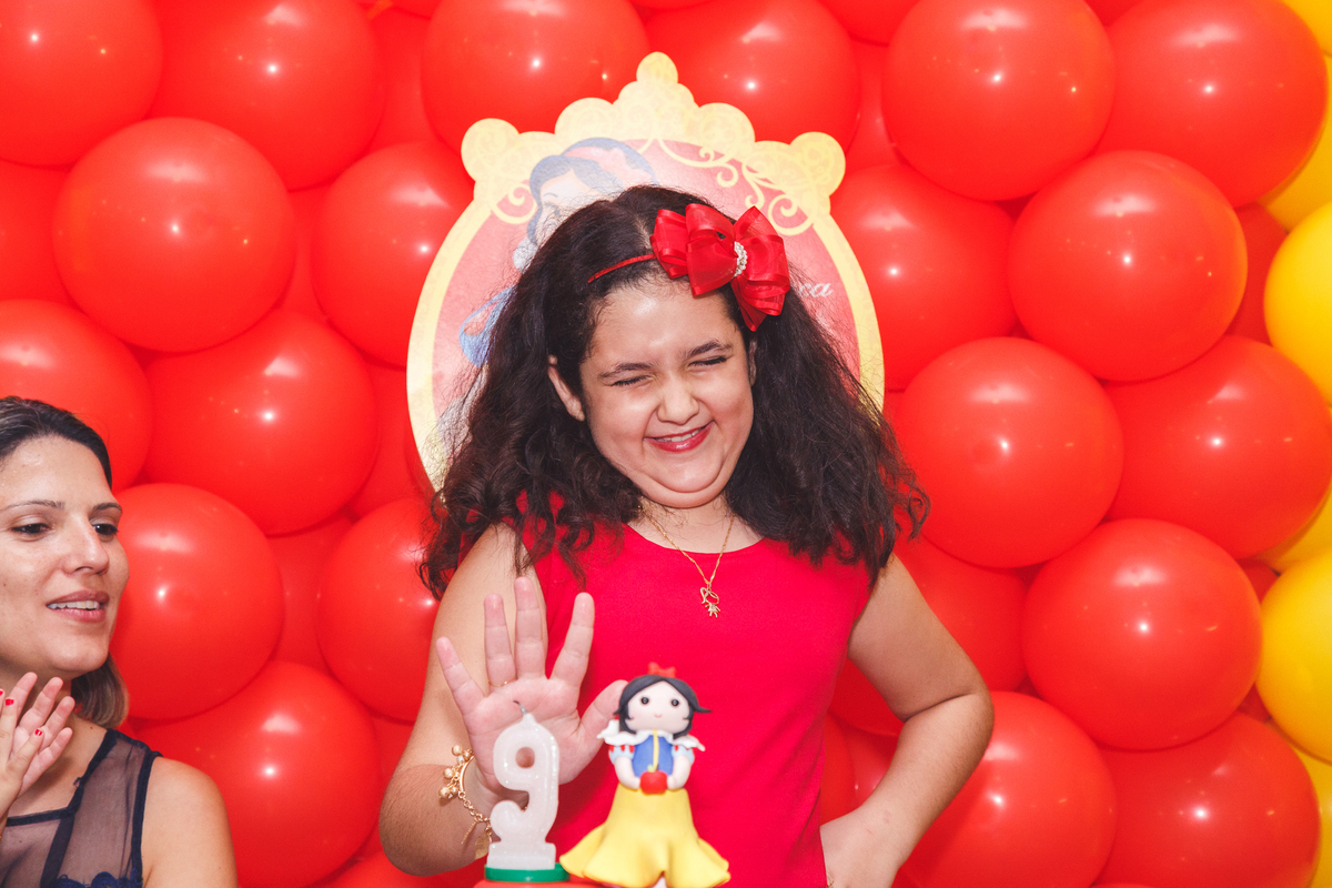 Criança atrás do bolo de seu aniversário rindo para a gracinha de um convidado.