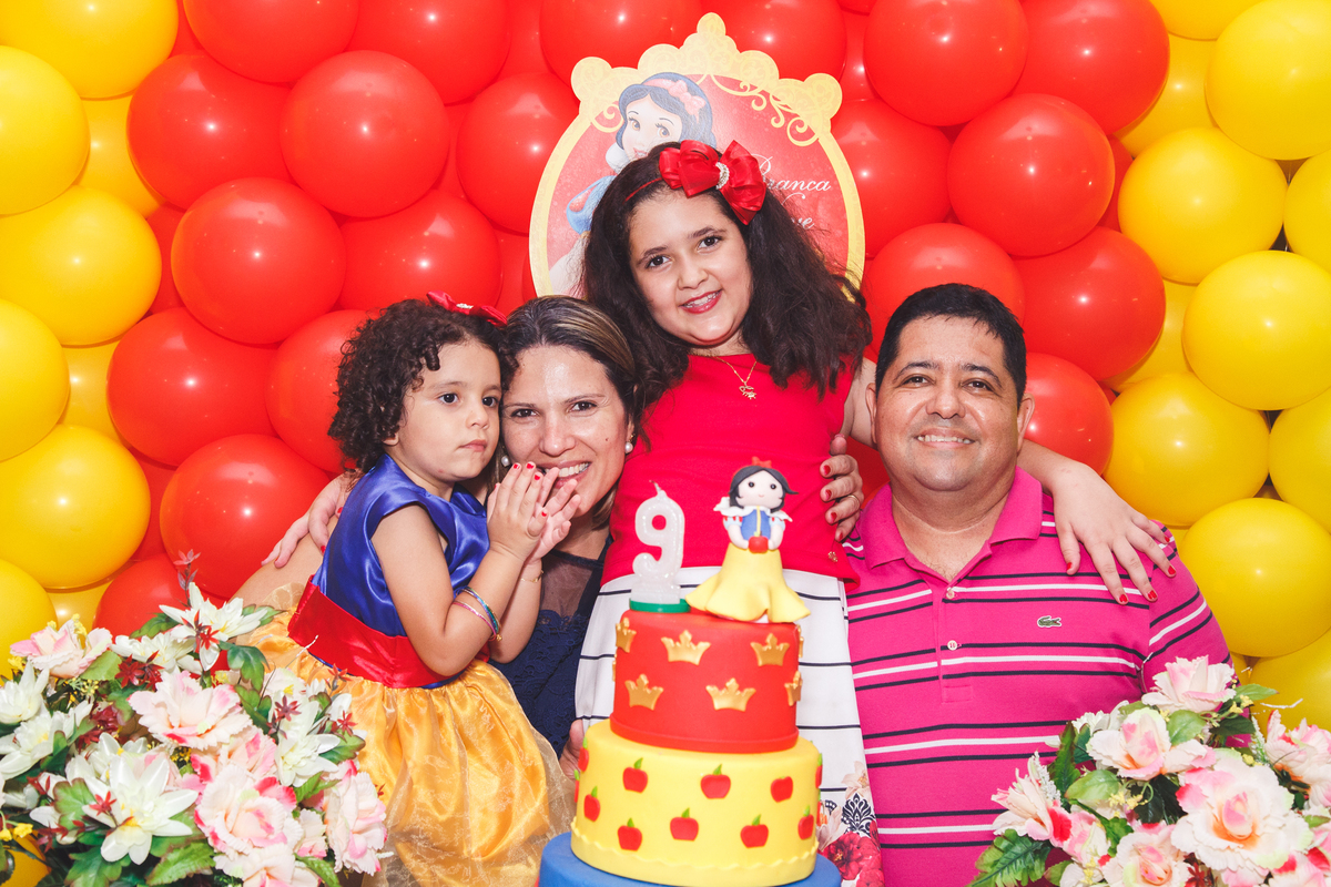 Família de pai, mãe e duas filhas reunida atrás da mesa do bolo após o parabéns na festa de aniversário das crianças.