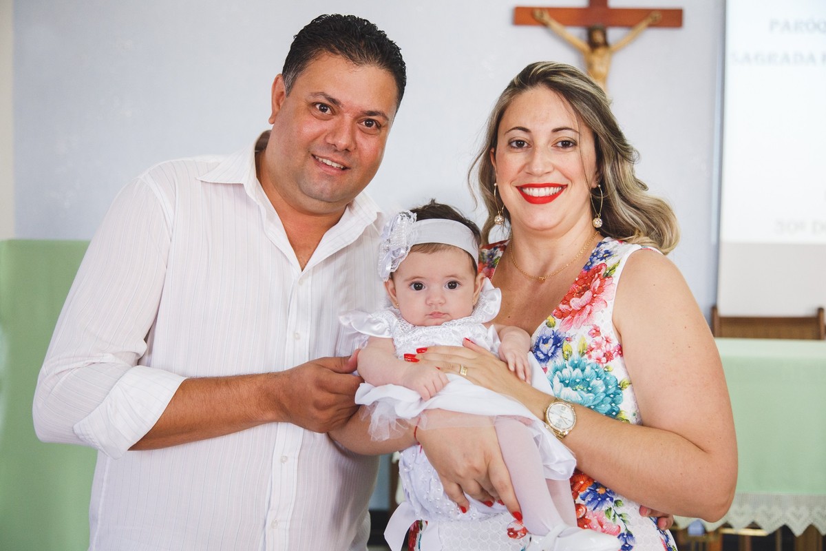 Pais de pé no altar carregando sua filha logo antes do início do seu batizado.