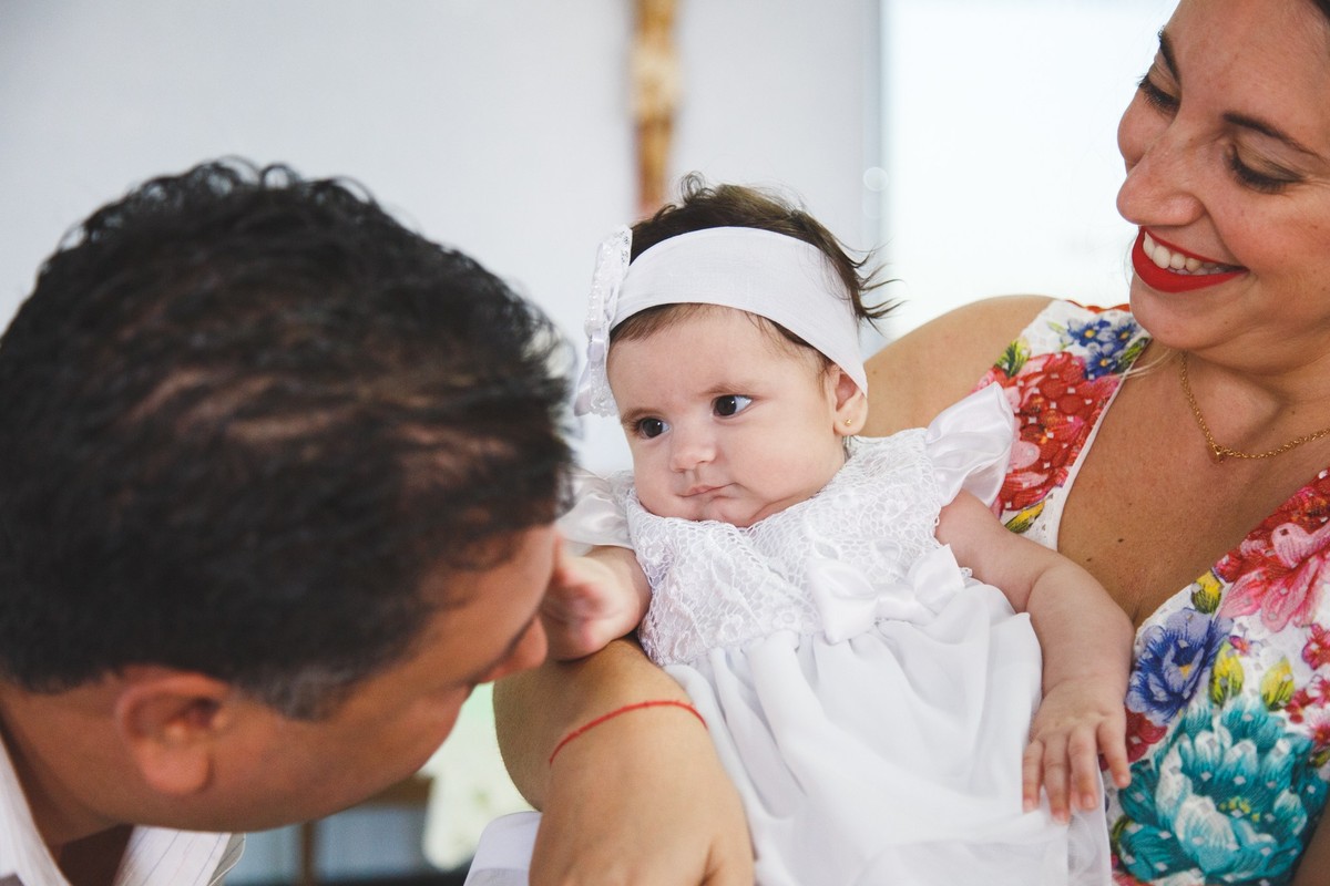 Bebê no colo de sua mãe, que sorri, olhando para seu pai e mexendo no rosto dele.