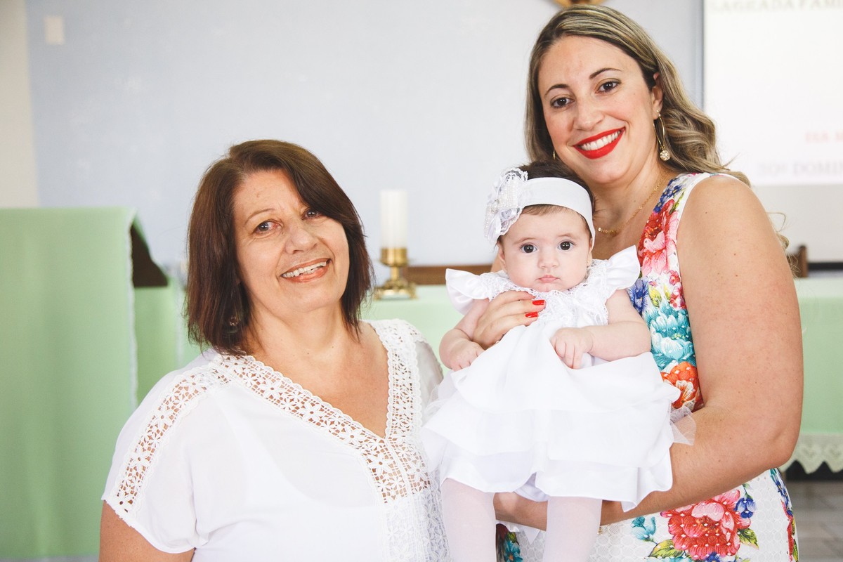 Três gerações, mãe, filha e neta no altar da igreja, aguardando o início do batizado da bebê.