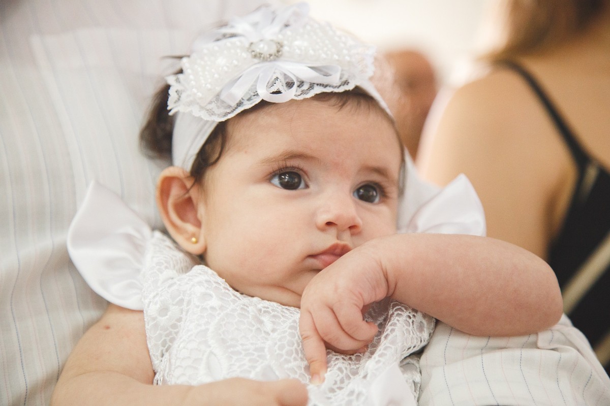 Close na bebê que está no colo de seu pai e observa os arredores com atenção.