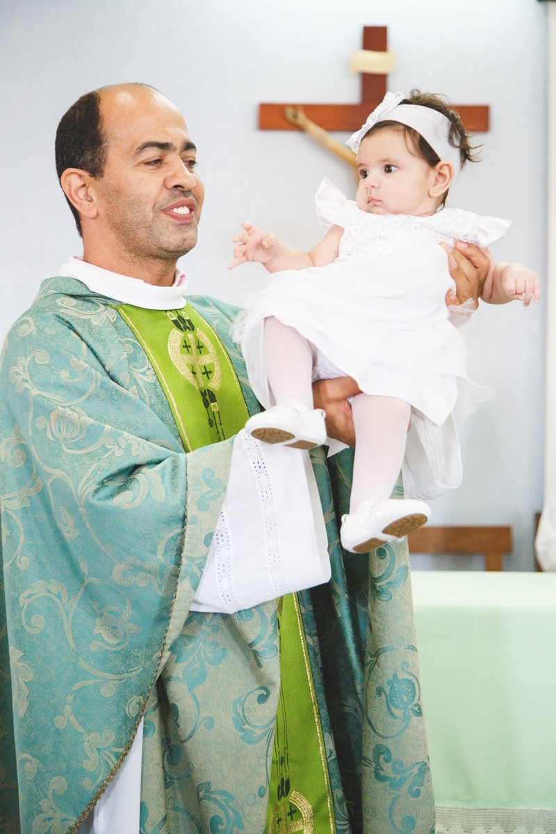 Padre com a bebê no colo apresentando ela para a congregação durante a cerimônia do seu batizado na igreja católica.