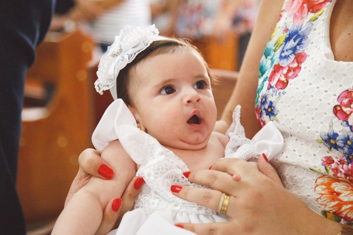 Bebê no colo da mãe após a bebê receber a unção com óleo abençoado durante a cerimônia de seu batizado.