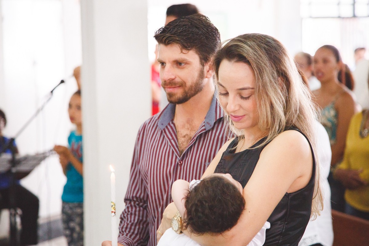 Padrinho e madrinha de consagração da bebê de pé durante a cerimônia de seu batizado.