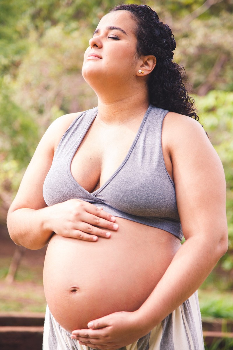 Gestante com as mãos na barriga, acariciando o bebê, e uma expressão pensativa, com os olhos fechados.
