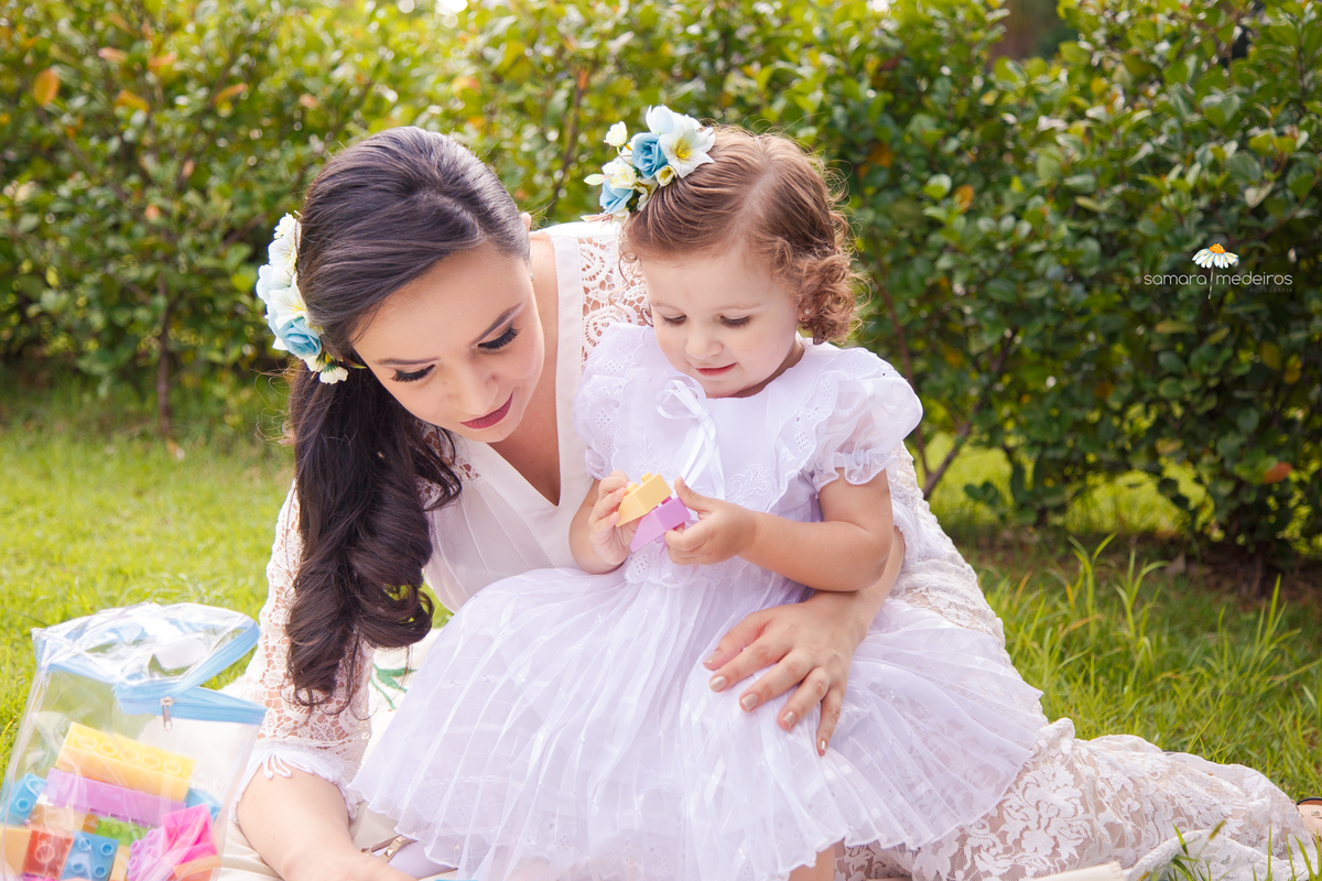 Criança e sua mãe sentadas na grama, sorrindo e brincando com blocos de montar.