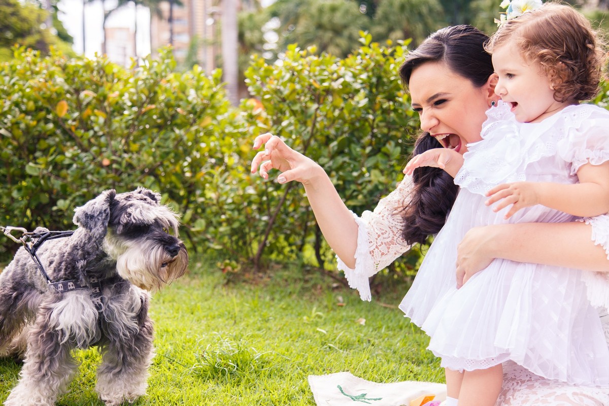 Mãe e sua filha sentadas na grama de uma praça de Belo Horizonte, brincando com um cachorro que apareceu durante o ensaio.
