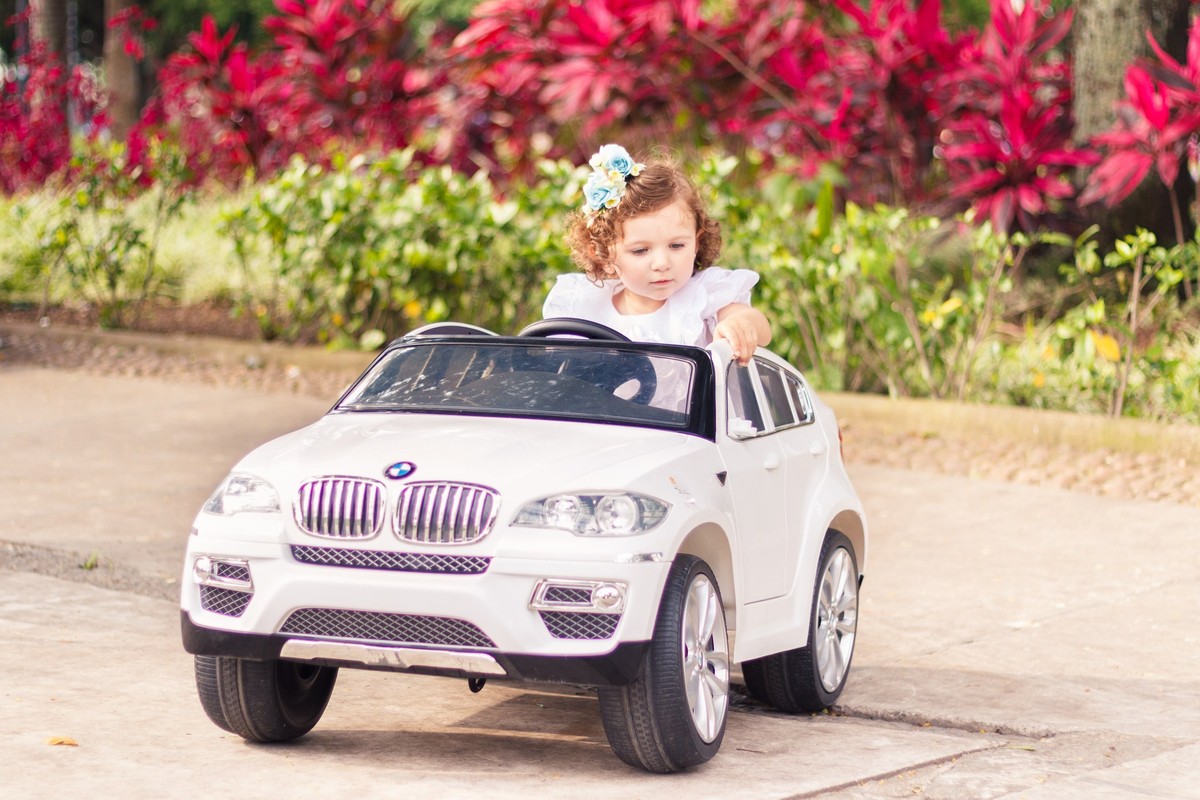 Criança dentro de um carrinho de brinquedo, com plantas coloridas ao fundo, em uma praça.