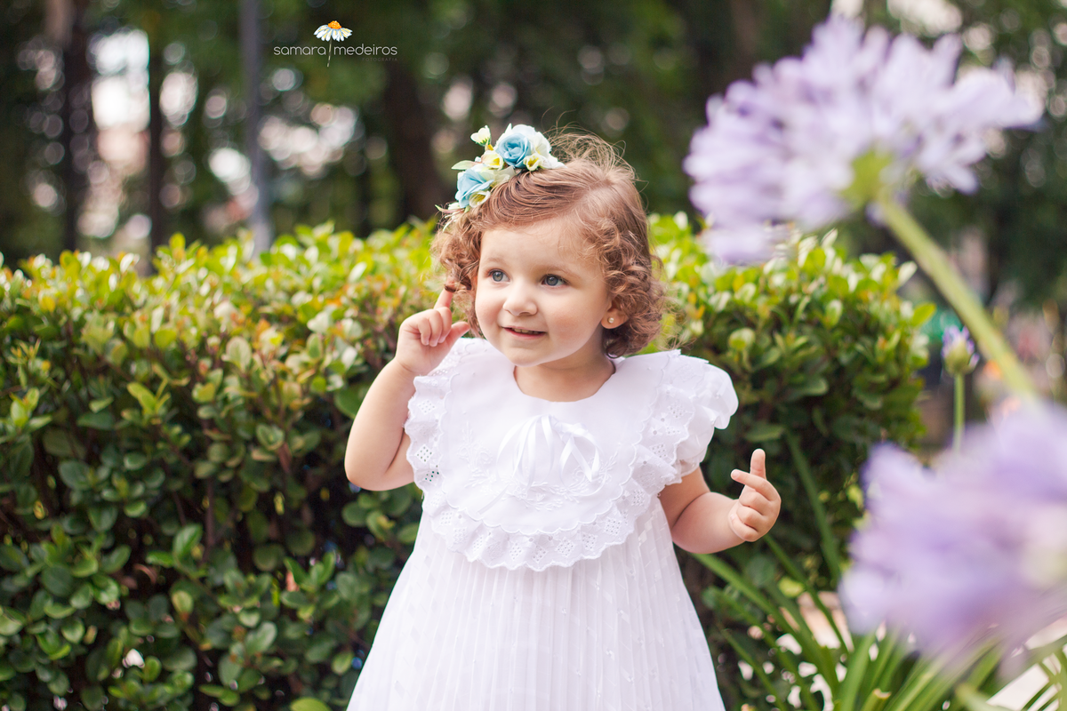 Criança em uma praça de Belo Horizonte, em meio a flores, apontando para o ouvido e com uma expressão atenta.